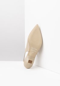 Scarpa beige a punta con una texture liscia, lati ritagliati e tacco quadrato piatto. Nome del marchio e taglia stampati sulla suola.