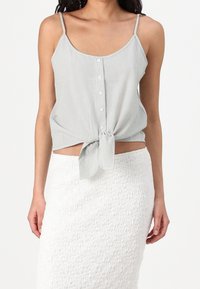 Szara jasnoszara koszulka na ramiączkach z paskowaniem, zapinana na guziki z przodu, zawiązana na supeł w talii, zestawiona z teksturowaną białą spódnicą.