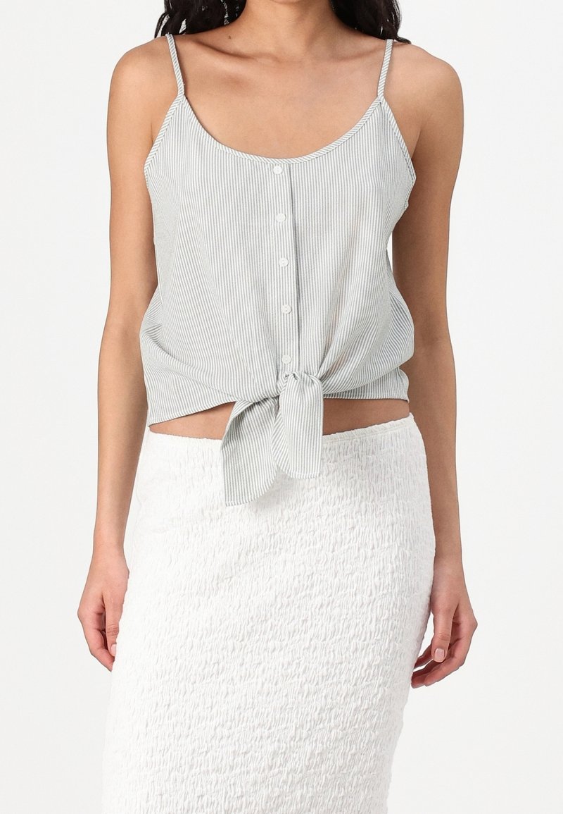 Szara jasnoszara koszulka na ramiączkach z paskowaniem, zapinana na guziki z przodu, zawiązana na supeł w talii, zestawiona z teksturowaną białą spódnicą.