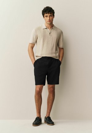 Beežist kootud polosärk vertikaalsete triipudega, millele on lisatud mustad lühikesed püksid ja mustad paeltega kingad tekstureeritud tallaga.