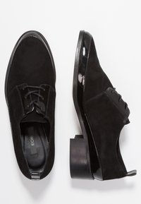 Czarne zamszowe buty na sznurowadłach z błyszczącymi akcentami z lakierowanej skóry, okrągłym czubkiem i słupkowym obcasem. Charakteryzują się teksturowaną cholewką i przeszyciami.