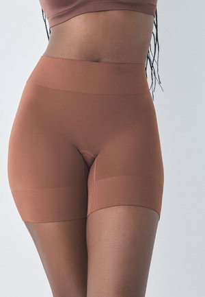 Femme portant un short de compression marron taille haute sans coutures et un soutien-gorge de sport assorti, montrant la zone médiane et le haut des cuisses.