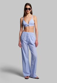 Valkoiset raidalliset bralette-toppi, jossa on säädettävät hihnat, yhdistettynä löysästi istuviin raidallisiin housuihin. Mallilla on päällä mustat aurinkolasit. Sileä kangas.