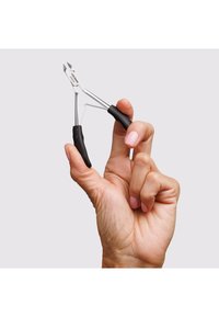 Hand holding small stainless steel cuticle nipper with black handles against plain light background.