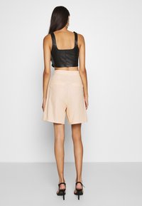 Top corto in pelle nera con scollatura quadrata abbinato a pantaloni corti beige chiaro con tasche laterali, texture liscia e vestibilità rilassata.