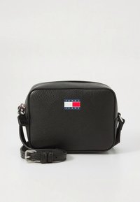 Zwarte leren crossbodytas met een rechthoekige vorm, een gestructureerd oppervlak en een rood-wit-blauw logo op de voorkant. Verstelbare riem.