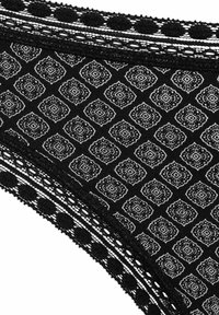 Zwarte stoffen slip met een wit diamanten patroon, verfraaid met delicate zwarte kantafwerking met stippen langs de randen.