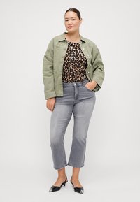 Chic green denim jacket, leopard print top, gray straight-leg jeans, and black heels with silver accents, all in a neutral background.