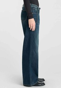 Donkerblauwe, wijde jeans gemaakt van denim. Bevat vijf zakken, riemlussen en een rechte snit. Gladde textuur en minimale hardware-details.