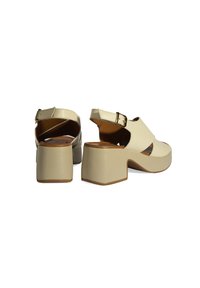 Beige block-heeled sandals with a cutout design. Features an adjustable strap with a gold buckle and a textured matte finish.