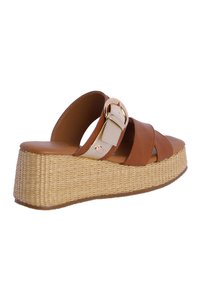 Sandalia de cuña de cuero marrón con dos correas cruzadas y una hebilla. Base de plataforma tejida texturizada. Diseño simplista y paleta de colores neutros.