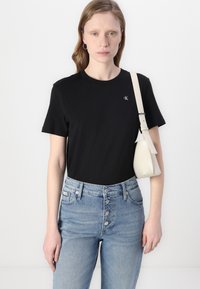 T-shirt noir à manches courtes avec un col rond et un petit logo, associé à un jean en denim bleu clair taille haute et un sac à main crème.
