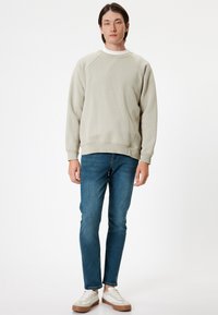 Ljust grå crew-neck tröja med raglanärmar, i kombination med blå slim-fit jeans och vita sneakers med bruna detaljer.