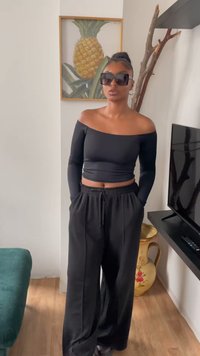 Melnā plecus atklājošā kroptopā, melnās platās bikses ar kabatām un lielām kvadrātveida saulessargiem. Gluda auduma, brīvs piegriezums.