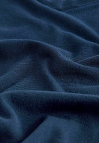 Tissu en maille douce bleu marine avec une texture lisse, présentant des plis et des rides légers, mettant en valeur sa nature légère et flexible.