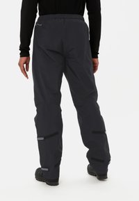 Pantalons noirs résistants à l'eau avec taille élastique, accents en velcro et ourlets inférieurs renforcés, conçus pour les activités de plein air.