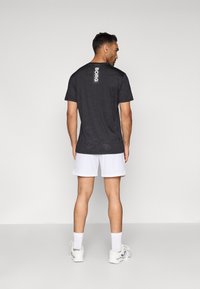 T-shirt preta de manga curta com um padrão subtil, apresentando um logótipo branco "BORG" nas costas, emparelhada com calções brancos e sapatilhas.