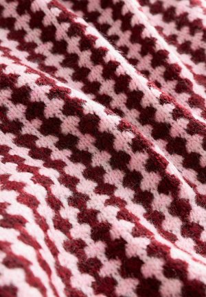 Tissu tricoté avec un motif pied-de-poule en rouge foncé et rose doux. Surface texturée avec des épaisseurs de fil variées et un aspect globalement flou.