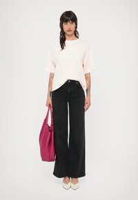 Czarne dżinsy o szerokich nogawkach w połączeniu z jasnor�óżowym, oversize'owym t-shirtem. Trzyma teksturowaną różową torbę i nosi białe buty z ostrymi noskami.