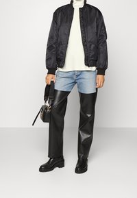 Czarna kurtka bomber, biała sweter, niebieskie dżinsy, czarne skórzane spodnie, masywne czarne buty oraz mała czarna torba.