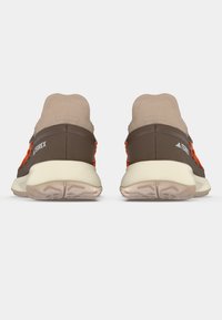 Chaussures de sport marron avec une tige beige et un détail de laçage orange. Surface texturée et semelle de couleur claire. Marquage sur le talon.