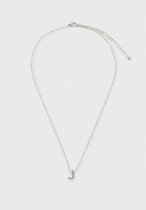 Collier chaîne argentée avec un petit pendentif en lettre cursive J et un fermoir ajustable sur fond blanc.