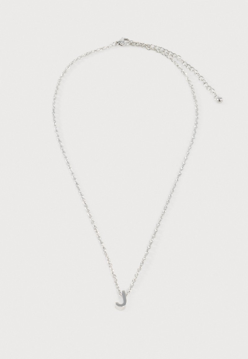 Collier chaîne argentée avec un petit pendentif en lettre cursive J et un fermoir ajustable sur fond blanc.