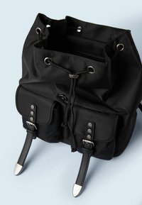 Svart tygryggsäck med snörstängning, framflikar, tryckknapp och silverfärgad hårdvara; har justerbara remmar och en slät textur.