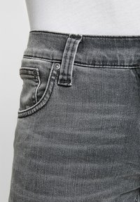 Grå denimjeans med en tät design, som har en framsida ficka, bältesöglor och en subtil vävd struktur med en blekt finish.