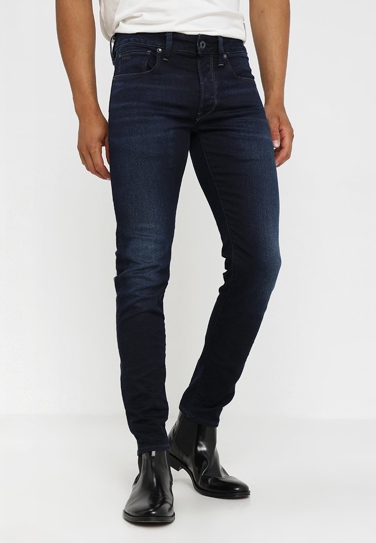 Mörkblå denimjeans med slim fit, som har en klassisk femficksdesign och subtila blekningar. Bärs med svarta ankelskor.