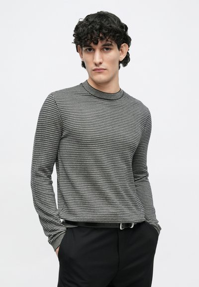 Fekete-fehér mintás hosszú ujjú póló kerek nyakkivágással és bordázott mandzsettákkal, fekete nadrággal párosítva, hogy laza megjelenést biztosítson.