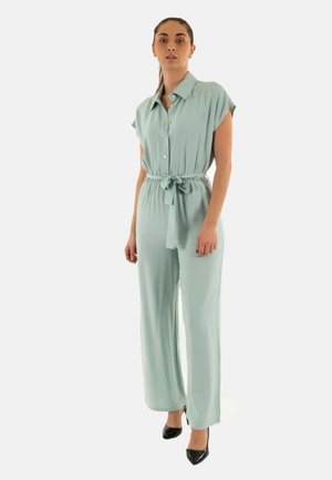 Mono verde claro con cuello de camisa, mangas cortas, cinturilla ceñida y corte de pierna ancha. Combinado con tacones negros.