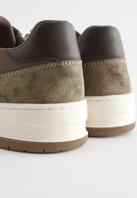 Brązowe zamszowe i skórzane sneakersy z teksturowanym tyłem, z białą grubą podeszwą i widocznym szwem.