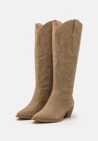 Knöchelhohe beigefarbene Wildleder-Cowboy-Stiefel mit spitzen Zehen, die über aufwendige Stickmuster, einen Blockabsatz und Ziehpullis an der Oberseite verfügen.