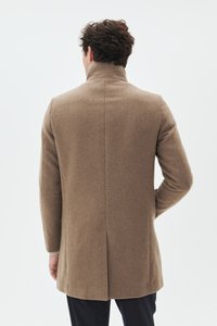 Manteau en laine marron avec col haut, coupe ajustée et fente unique au dos. Texture lisse et lignes épurées sans ornements.