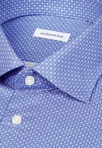 Jasnoniebieska koszula w drobny wzór z małymi białymi kółkami, z kołnierzem rozstawionym i dwoma białymi guzikami przy szyi. Metka widoczna wewnątrz kołnierza.