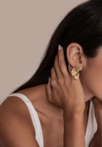 Pendientes en tono dorado con un diseño de hojas superpuestas y texturizadas. La forma es orgánica y audaz, reflejando la luz con un acabado brillante.