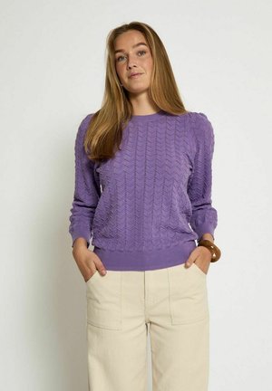 Pull en maille violet avec un motif de vagues texturé, encolure ronde, et poignets et ourlet côtelés. Associé à un pantalon large beige.