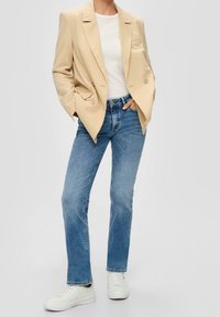 Béžový blazer se pruhy přes bílý top, v kombinaci se světle modrými rovnými džínami a bílými teniskami. Hladký materiál a dobře padnoucí střih.