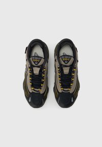 Μαύρα και μπεζ αθλητικά παπούτσια με υφασμένο πάνω μέρος, κίτρινες κορδόνια, ανακλαστικές λεπτομέρειες και μαλακή σόλα, με το λογότυπο '1000'.