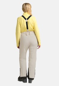 Beige sneeuwbroeken met verstelbare zwarte bretels, voorzien van zijritsen en een getailleerde taille voor comfort, gecombineerd met een gele fleece top.