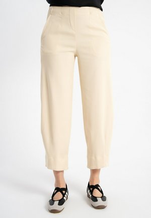 Beżowe spodnie z wysokim stanem, szerokimi nogawkami skrócone, noszone z czarno-szarymi butami z krzyżującymi się paskami.