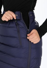 Marine blauwe pufferrok met horizontale stiksels, ritssluiting aan de voorkant en drukknoop. De stof lijkt glad en geïsoleerd.