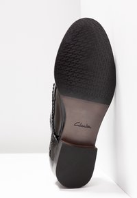 Semelle d'une chaussure habillée en cuir noir avec avant-pied en caoutchouc texturé, milieu de semelle lisse, talon empilé et logo « Clarks » embossé sur la voûte plantaire.