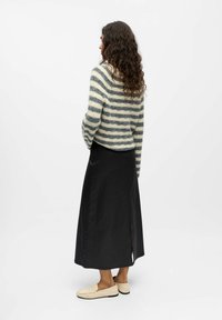 Randig tröja i off-white och marinblå, med avslappnad passform. Svart lång kjol med en sidav slit, tillsammans med beiga loafers.