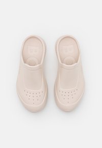 Paire de sabots en caoutchouc beige avec des trous de ventilation sur le dessus et des semelles intérieures texturées, vue de dessus sur un fond blanc.