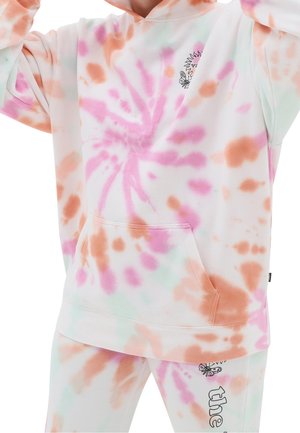 Persona vistiendo una sudadera con capucha y pantalones blancos con patrones de tie-dye en rosa, naranja y verde claro, con pequeños gráficos de sol y mariposas.