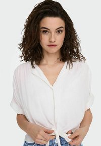 Chemise blanche à manches courtes et boutonnée avec un lien à la taille, fabriquée en tissu léger, présentant une texture lisse et une coupe décontractée.