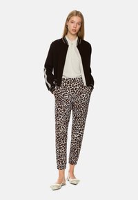 Black bomber jacket with white stripes, white blouse, and beige leopard-print pants. Beige slingback flats with bow detail. Minimalistic design.