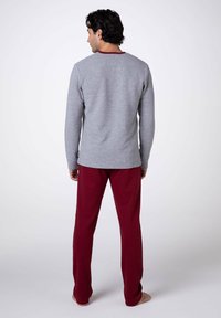 Maglietta a maniche lunghe grigia con trama a coste e colletto color amaranto, abbinata a pantaloni color amaranto. Vestibilità comoda e tessuto morbido, vista da dietro.